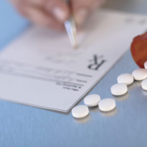 Doctor writing prescription on pad next to pill bottle