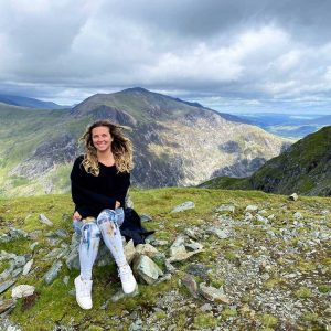 Emily Qureshi-Hurst sitting in scenic field with mountains behind