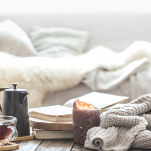 Still-life home comfort in the living room with a cup of tea, a lit candle, and a knitted sweater.