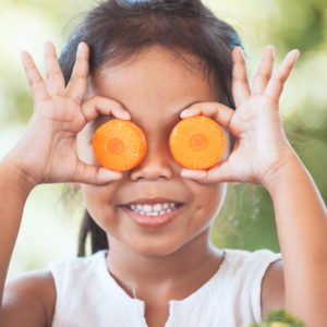 Cute little girl holds carrot rounds up to her eyes as a joke.