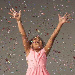 Young girl in party dress celebrating with confetti