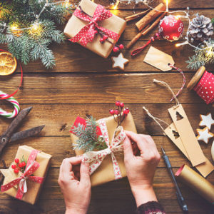 Top view of a woman's hands wrapping homemade Christmas holiday presents in craft paper with ribbon on wooden table