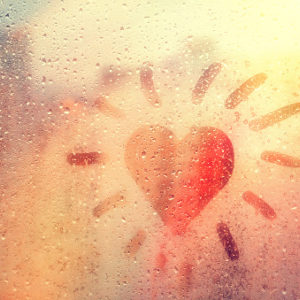 Hand-drawn orange, heart-shaped like sun on rainy window