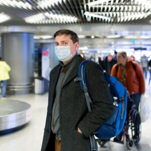 Man in gray coat wearing protective disposable medical mask in airport during spread of N-CoV 2019 influenza coronavirus