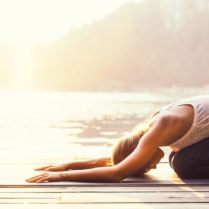 Woman in childs pose by lake