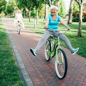 Happy senior couple riding their bikes in the park, playfully lifting their legs up as they ride