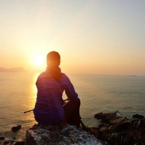 Woman sits on rock and watches sunset