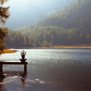 Woman practicing meditation and yoga at sunset on a pier on a forest lake