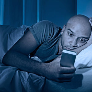 Man staring at smartphone in bed at night