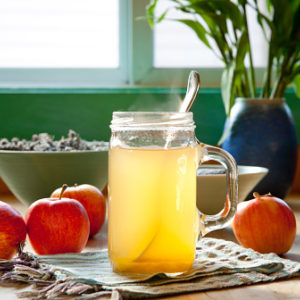 Hot apple cider vinegar and honey drink with apples on a table