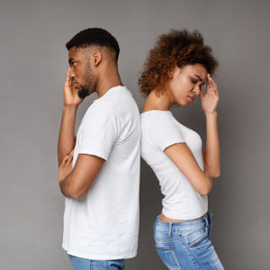 Upset couple standing back to back in front of gray background