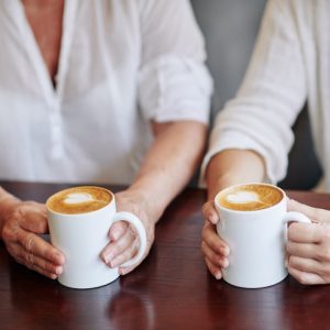 two women drink coffee together at a table