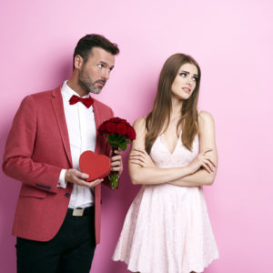 Man offering woman flowers and chocolate. Woman is disdainful.