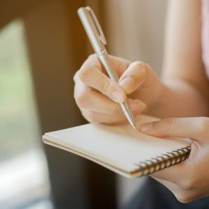 Closeup of woman's hands writing on a notepad