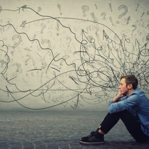 Young man sitting on the ground surrounded by anxious thoughts.