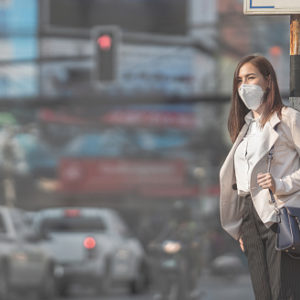 Woman dressed in business attire wearing air mask as she waits to cross the street