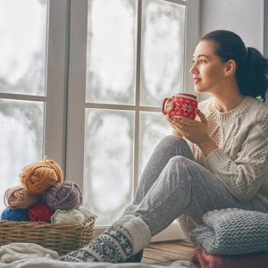 Woman sitting in silence drinking coffee by window in contemplation during holiday season