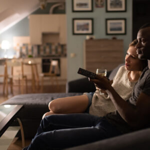 Couple watching a movie or TV show at home on couch, with bottle of wine.