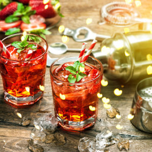 Red drink garnished with mint and candy cane next to cocktail shaker