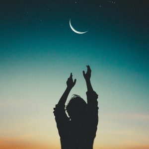 Silhouette of person reaching up to moon