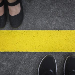 Two pairs of shoes on opposite sides of yellow line to symbolize boundaries