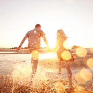 A couple holdings hands splashes through the tide