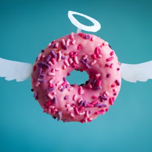 sweet pink donut with white paper wings and nimbus on a blue background