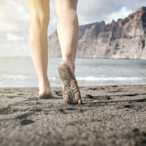 woman walking on the beach barefoot to stay grounded