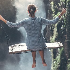 Woman on large wooden swing swinging over a waterfall