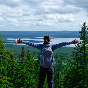 Woman with backpack on in the woods, arms stretched toward the sky