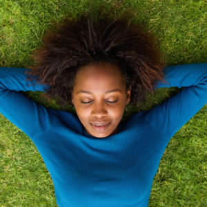 Black woman enjoying a guided meditation on a patch of green grass, feeling soothed and uplifted