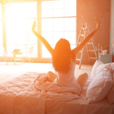 Woman stretching in bed with sunlight