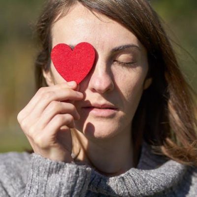 woman holding heart-shaped paper cut out over her eye