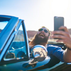 bearded man taking selfie while driving car