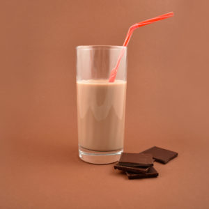 Chocolate milk with chocolate pieces. Glass of chocolate milk on a brown background.