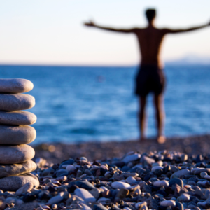 Man on beach with open arms and balancing stones