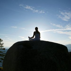 Woman meditating on large rock