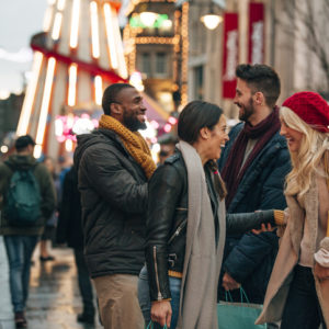 Side view of two couples meeting on a city street. It's winter and there is a fair ground ride on the street.