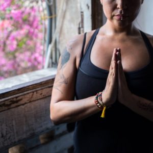 Woman with tattoos holds hands in anjali mudra