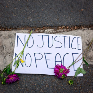 No Justice, No Peace sign lays on pavement with flowers around it