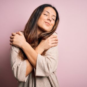 Woman hugging herself and smiling as a self-love practice