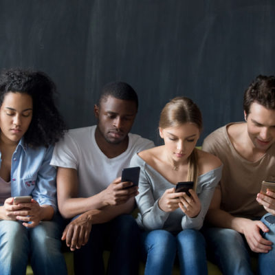 Young people sitting on couch, ignoring each other, using applications in smartphones.