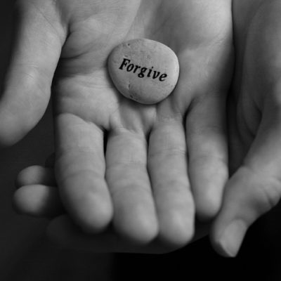 A hand holding a smooth stone that reads "forgive."