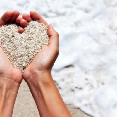 Woman holding sand in heart shape on beach