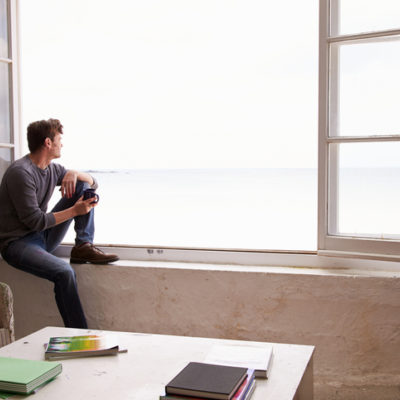 Man, isolated, looks out onto the water from his window