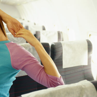 Woman in airplane with hands behind head, eyes closed