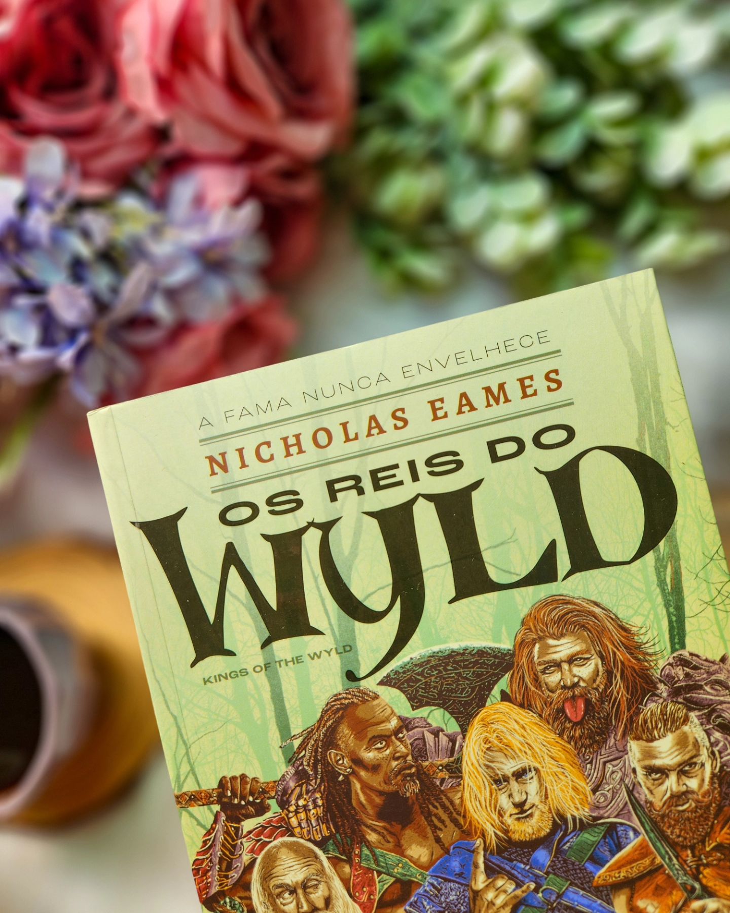 📖 "Clay havia muito desconfiava que a história era só isso: uma história. Um jeito de dar sentido a um mundo sem sentido."⁣
⁣
Nicholas Eames faz sua estreia e que estreia! Os Reis do Wyld é aquele livro que você simplesmente não consegue largar até chegar ao fim . Aconteceu isso comigo, me viciei nessa narrativa bem humorada e sarcástica!⁣⁣
⁣⁣
Clay um grande e famoso guerreiro, agora vive dias tranquilos com sua esposa e filha. Ele é conhecido pela alcunha "Mão Lenta" quando estava em seus momentos de glória junto com seu bando, o Saga, eles eram conhecidos como " Os reis do Wyld".⁣
⁣
 Clay é pego de surpresa quando seu antigo companheiro de batalha Gabriel aparece. Metade do homem que foi, Gabriel quer reunir novamente o bando, ele já quis fazer isso em outras ocasiões e Clay já está com a resposta na ponta da língua: Não.⁣
⁣
 Ele não pretende deixar suas meninas para viver perigosamente. Mas dessa vez as coisas são diferentes, a filha de Gabriel precisa de ajuda e rápido. ⁣⁣
⁣⁣
Rose, a filha de Gabriel se tornou uma guerreira e uma mercenária famosa por encarar missões difíceis, assim como seu pai. Gabriel era o líder do bando, sua história é conhecida por todo lugar, existem músicas sobre ele. ⁣
⁣
O bando está aposentado, porém suas histórias de grandes batalhas e monstros vencidos ainda são amplamente conhecidas e comentadas. Gabriel imagina que apenas reunindo seus antigos companheiros de luta, poderá ter sucesso no resgate da filha.⁣⁣
⁣⁣
Quando o restante do bando é inserido na narrativa fica impossível de não simpatizar e amar cada um deles. Moog que é um mago, Matrick, rei e Ganelon o sério. Na verdade percebi que Clay é mais na dele, Gabriel como mencionei, não está mais em seus momentos de glória, Moog é brincalhão, mas passou por momentos difíceis e dolorosos e Ginelon sempre está metido em situações pra lá de malucas.⁣⁣
⁣
⇣ 𝐂𝐨𝐧𝐭𝐢𝐧𝐮𝐚