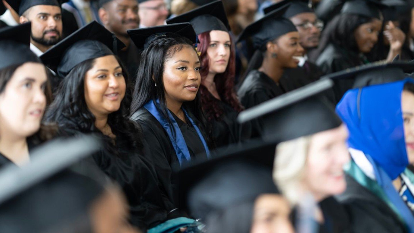 Graduates smiling in rows wearing caps and gowns during commencement ceremony.