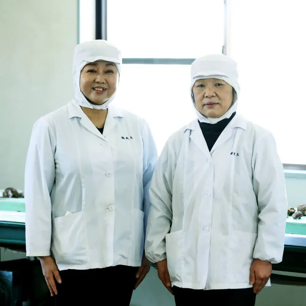 Two TAKEHISA staff in white hygiene coats and caps at the company's selection and packing facility