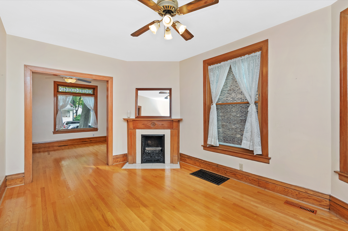 Before staging, this empty historic Evanston single-family home's dining room and living room were lacking any furnishings or art. The dining room has a fireplace, light maple hardwood floors, and white walls. This photo is part of a before/after series showcasing the power of home staging.